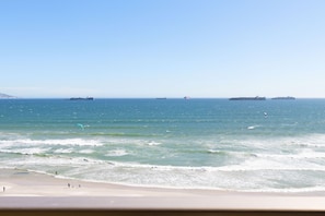 Une plage avec des vagues et des navires à l’horizon.