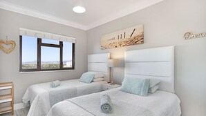 Een slaapkamer met twee bedden, een raam met uitzicht, een nachtkastje met lamp en een decoratie aan de muur.
