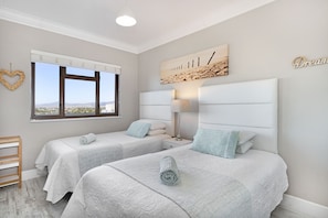 Une chambre avec deux lits, une fenêtre donnant sur un beau paysage, une table de chevet avec une lampe et un élément décoratif mural.