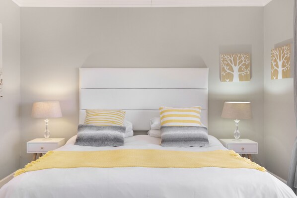 A neatly made bed with white and yellow bedding, two bedside tables with lamps, and wall art. - Witsand 804 (Cape Town)