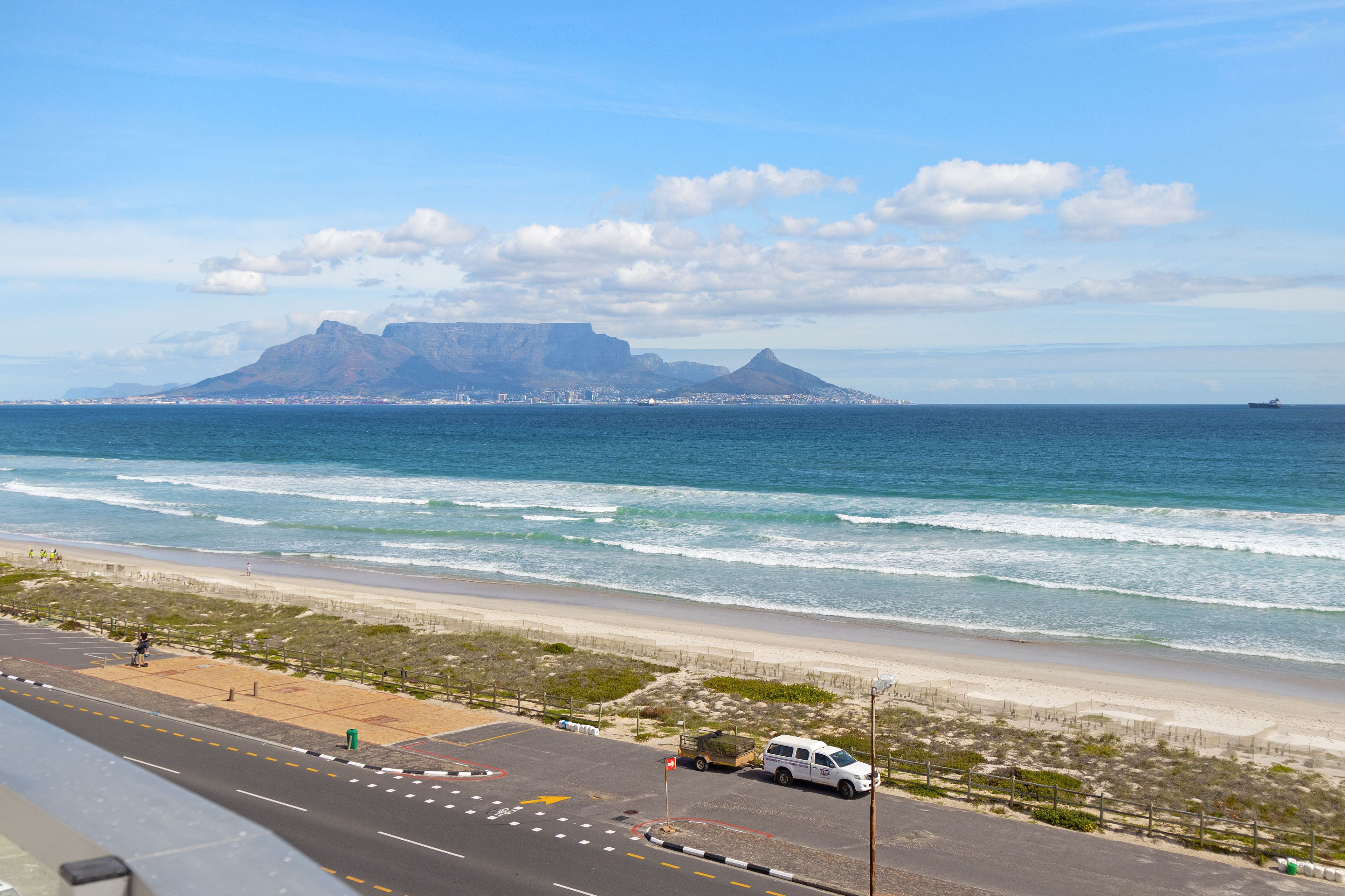 A coastal road with a beach and mountains in the background.