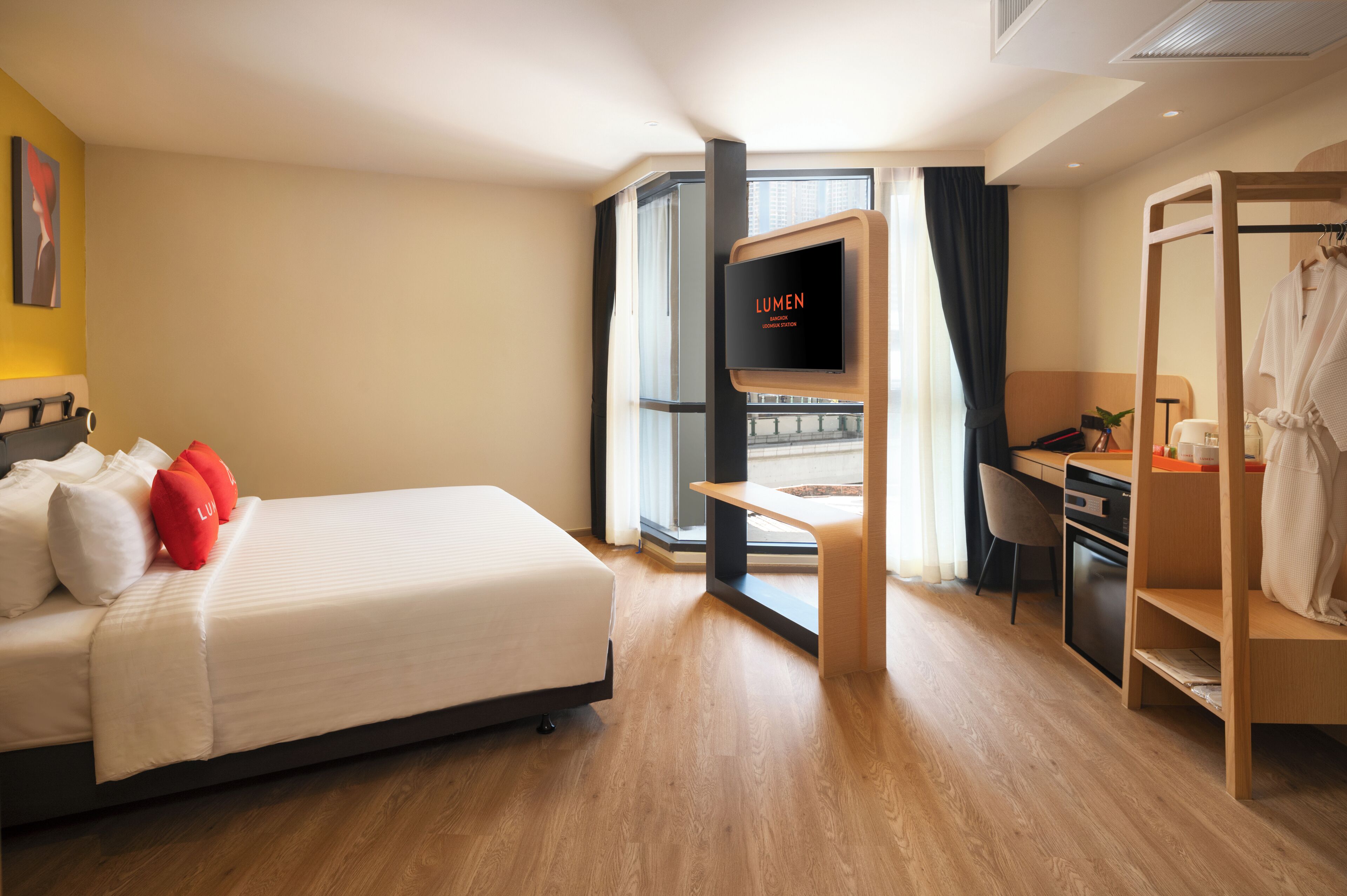A modern hotel room with a bed, a desk, a TV, and a view of the city.