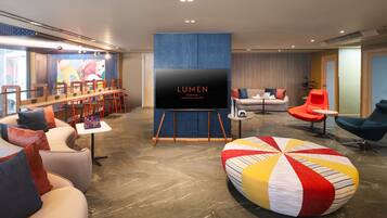 A modern hotel lobby with a large flat-screen TV, comfortable seating areas, and a colorful wall mural.