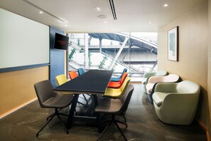 Un salón de conferencias con una larga mesa, varias sillas y un amplio ventanal con vista a una escalera mecánica.