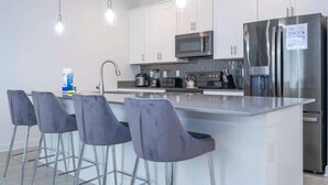 Una cucina moderna con mobili bianchi, elettrodomestici in acciaio inossidabile e un'isola centrale con sgabelli da bar.