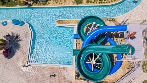 Vista aerea di una piscina con due scivoli e una zona solarium circostante.