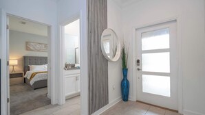 Un corridoio con una porta, uno specchio, un vaso blu e un letto sullo sfondo.
