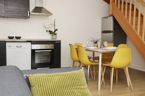 A compact kitchen with modern appliances, a dining area with yellow chairs, and a staircase.