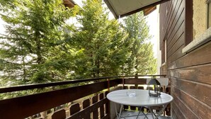 A balcony with a round table and a chair, surrounded by a wooden railing, overlooking a forested area. - Comfortable Studio Your Home Near Zermatt (Taesch)