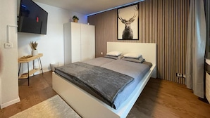 A modern bedroom with a bed, a TV mounted on the wall, and a decorative deer head on the wall. - Comfortable Studio Your Home Near Zermatt (Taesch)