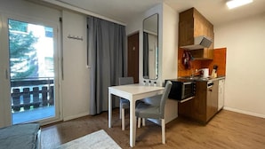 A compact living space with a kitchenette, a dining area, and a sliding glass door leading to a balcony. - Comfortable Studio Your Home Near Zermatt (Taesch)