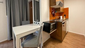A compact kitchenette with a stove, oven, and sink. There is a small dining table with chairs. - Comfortable Studio Your Home Near Zermatt (Taesch)