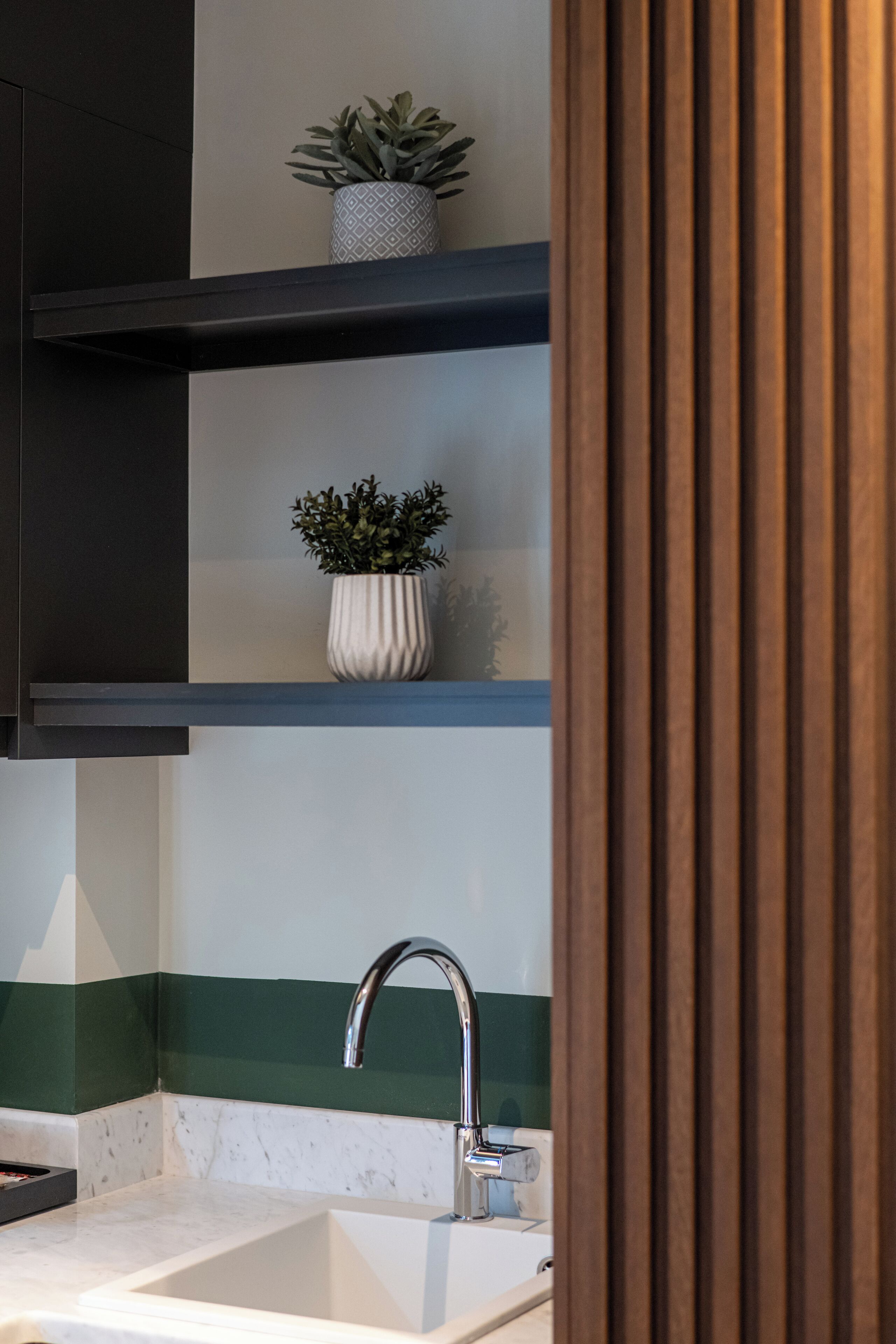 Una cucina moderna con un lavello bianco, un rubinetto in acciaio inossidabile e due ripiani con piante in vaso.