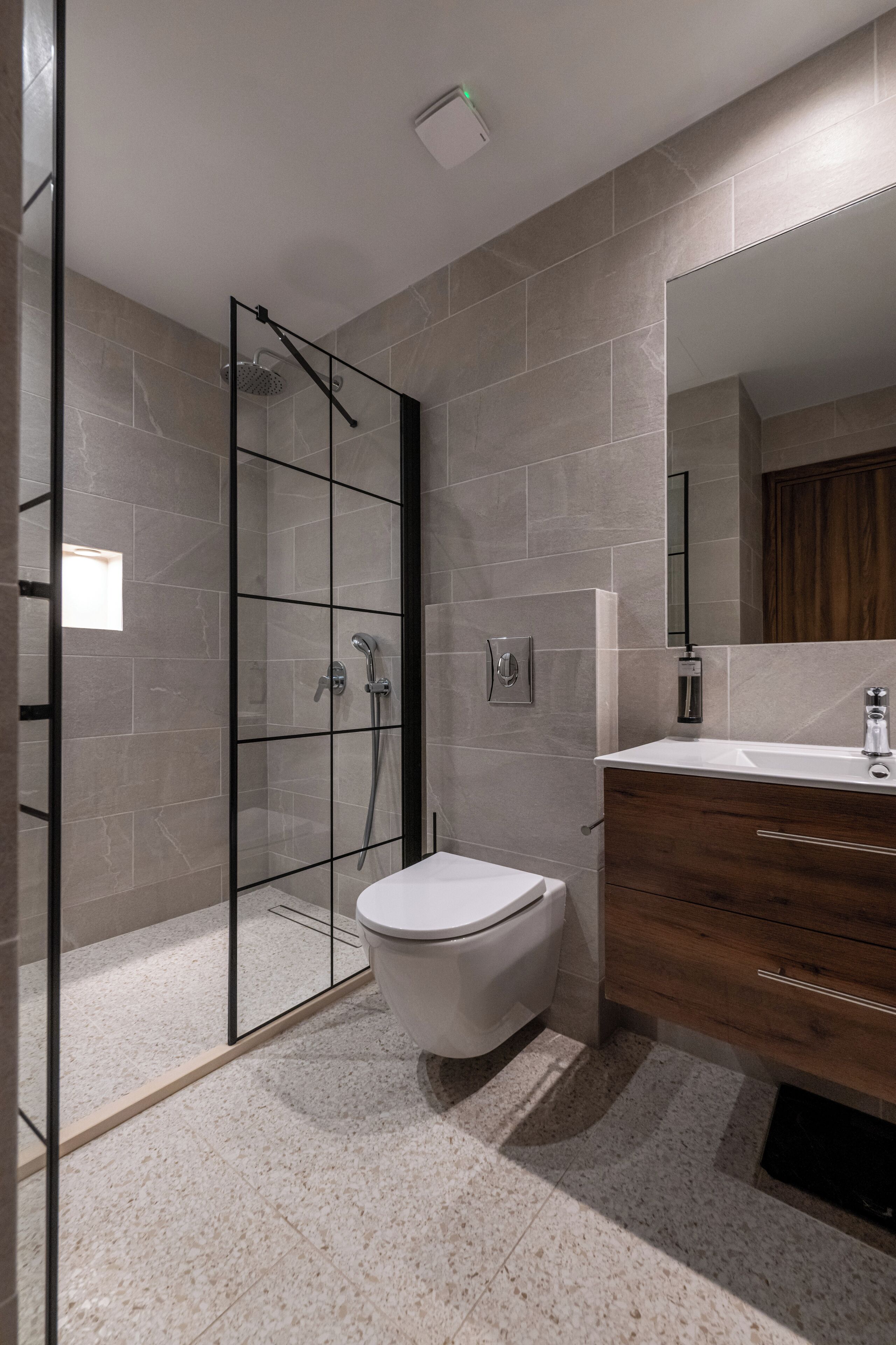 A modern bathroom with a glass-enclosed shower, a white toilet, and a wooden vanity with a mirror.