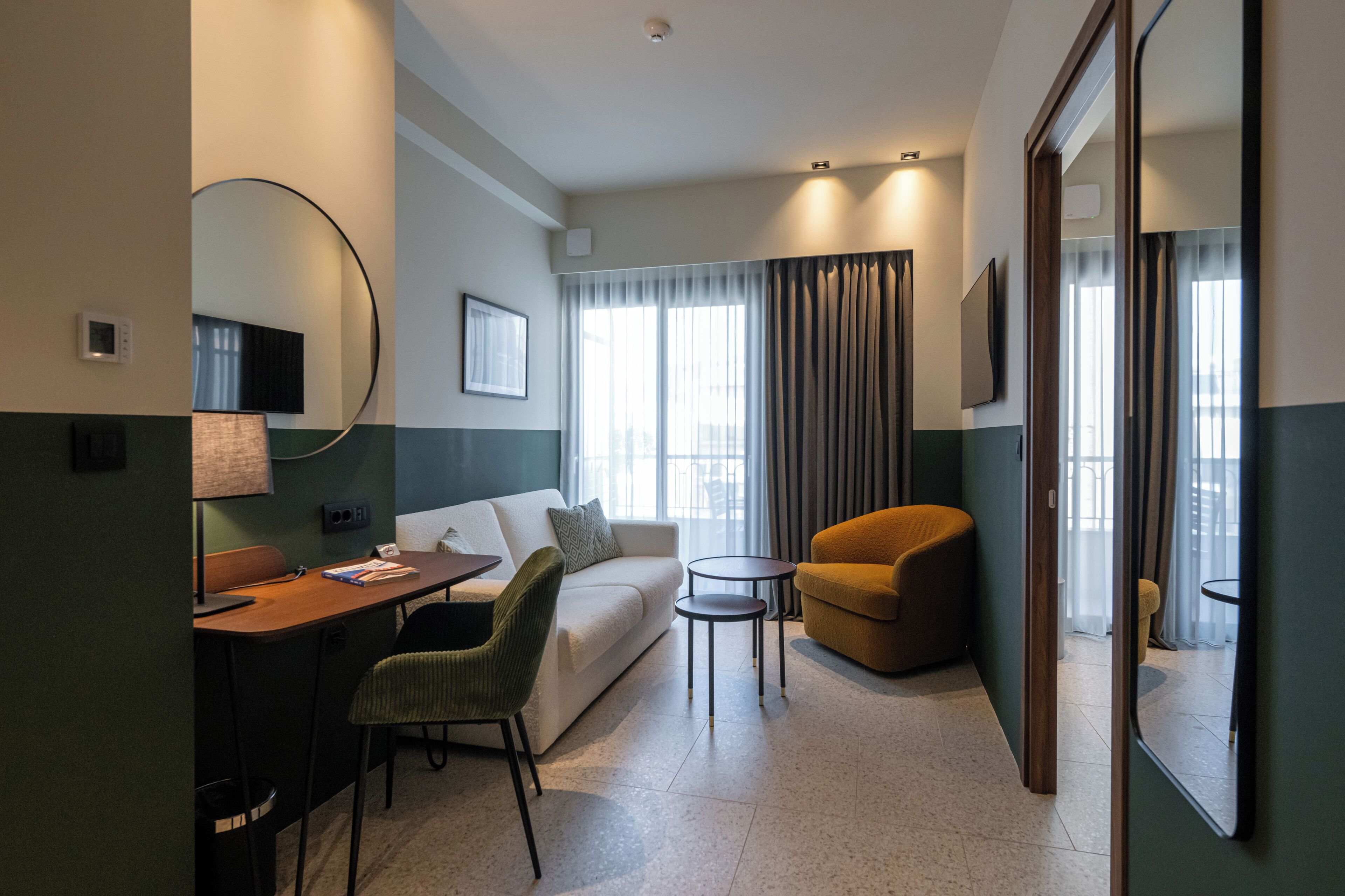 Une chambre d’hôtel comprenant un lit, un canapé, un bureau avec une chaise, une petite table et un miroir.