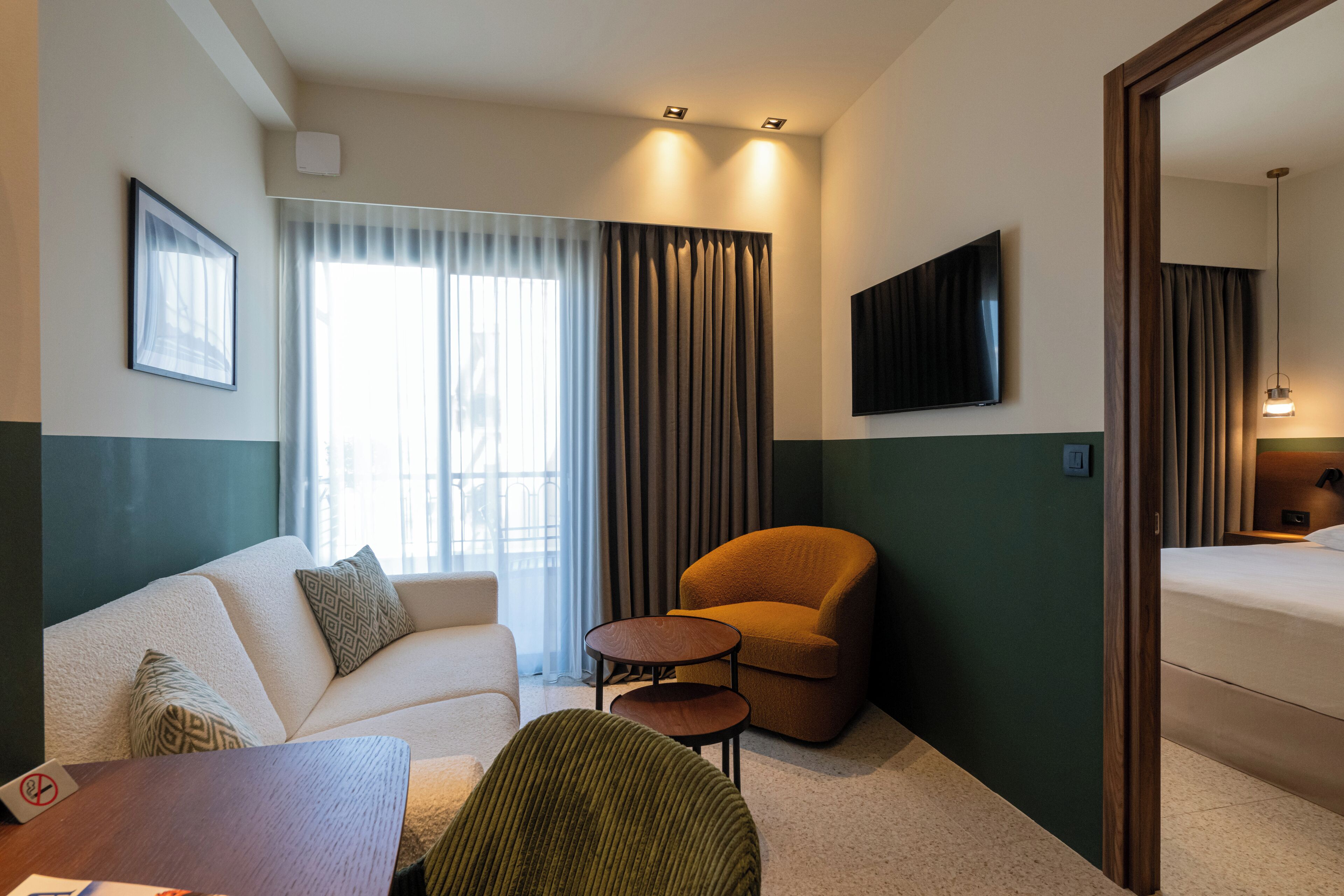 A hotel room with a sofa, armchair, small side table, and a bed.