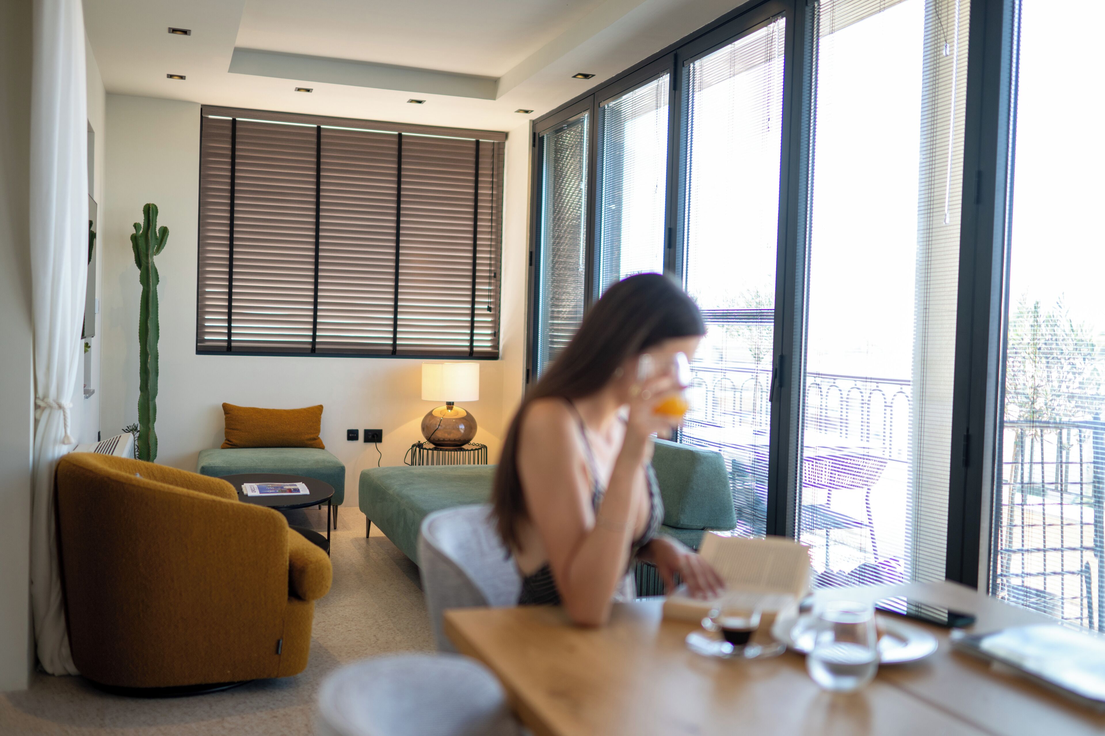 Een moderne woonkamer met een bank, een tafel met een drankje en een raam met zonwering.