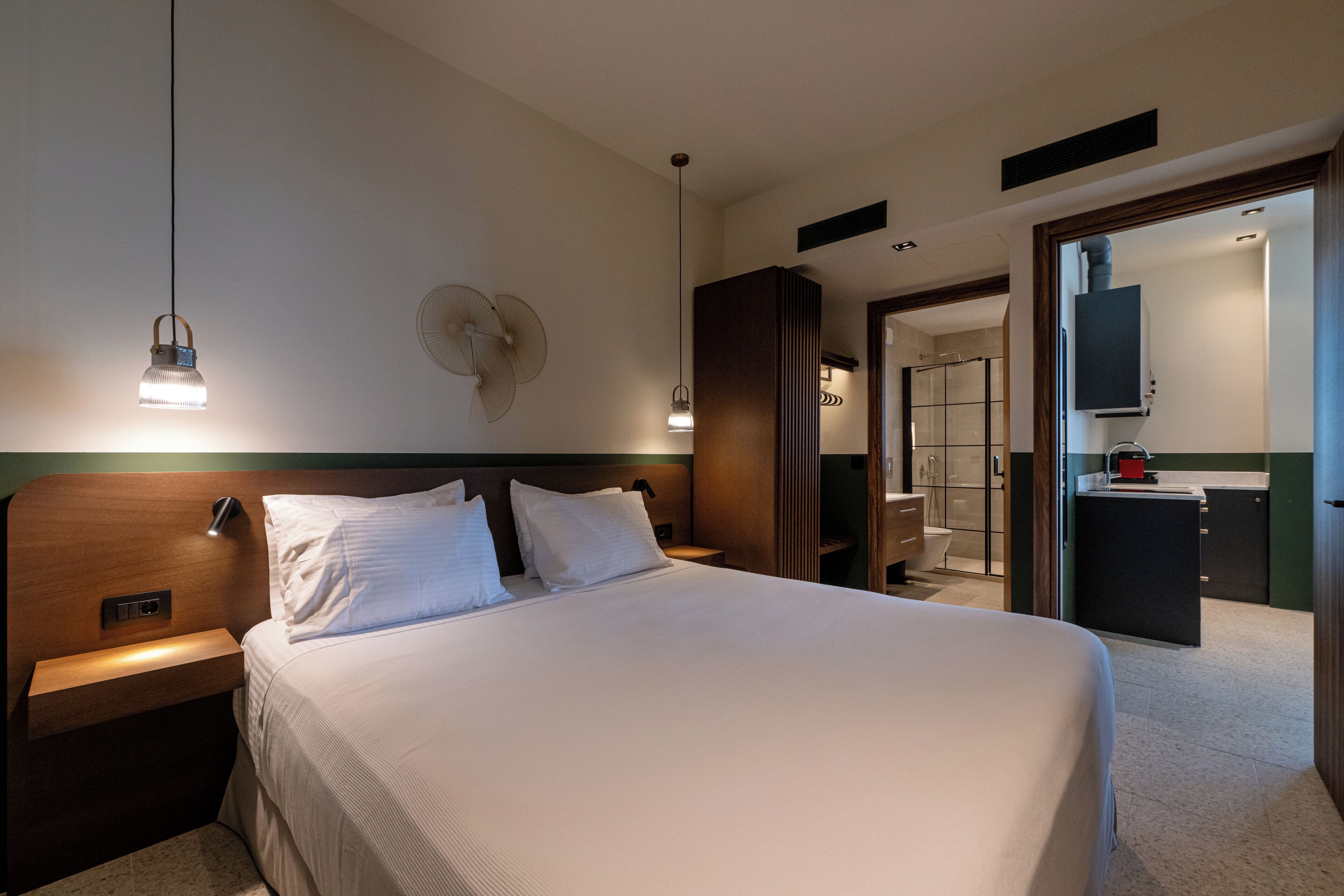 A hotel room with a large bed, bedside tables, a wall-mounted fan, and a bathroom visible through an open door.