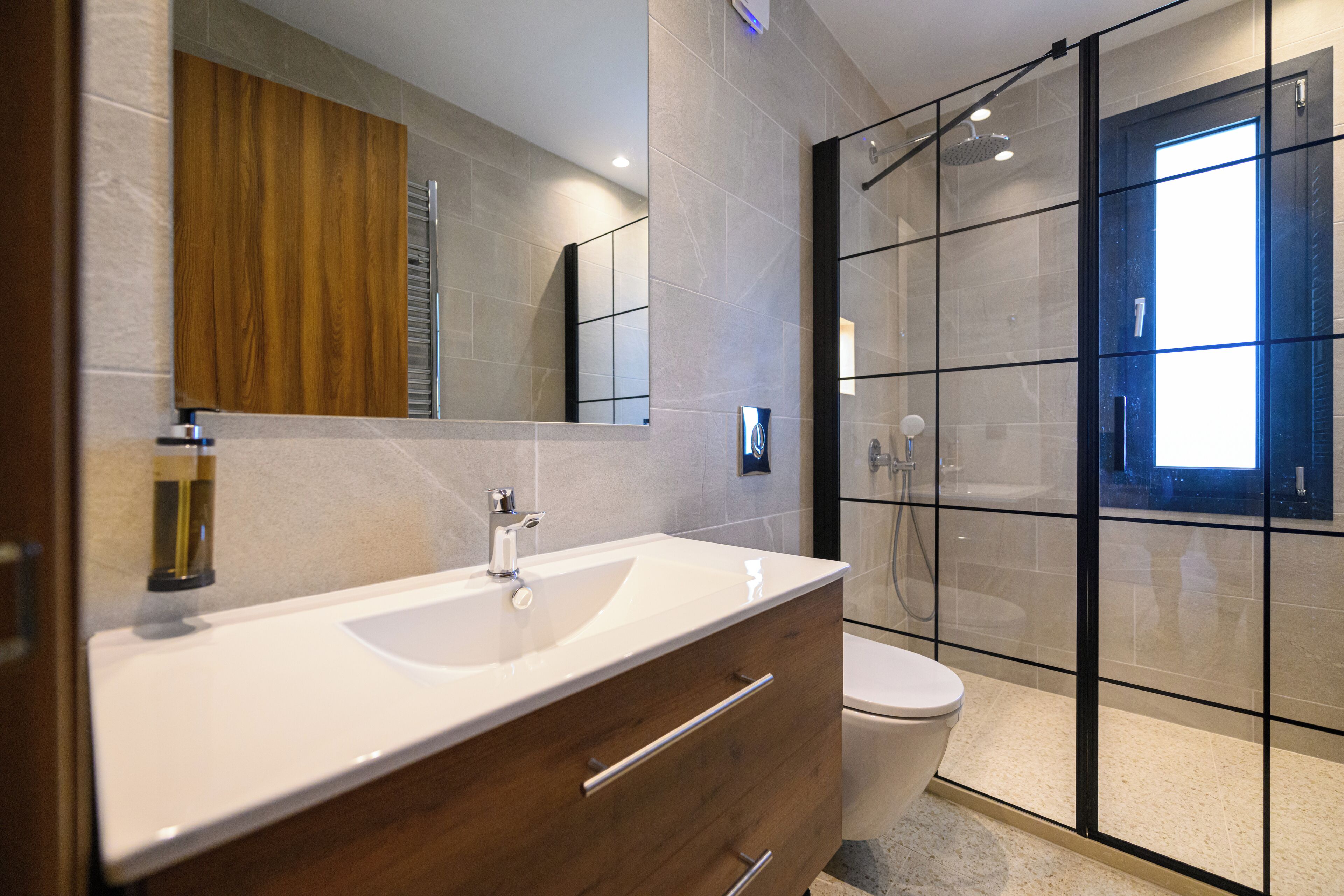 A modern bathroom with a wooden vanity, a large mirror, a glass shower enclosure, and a toilet.