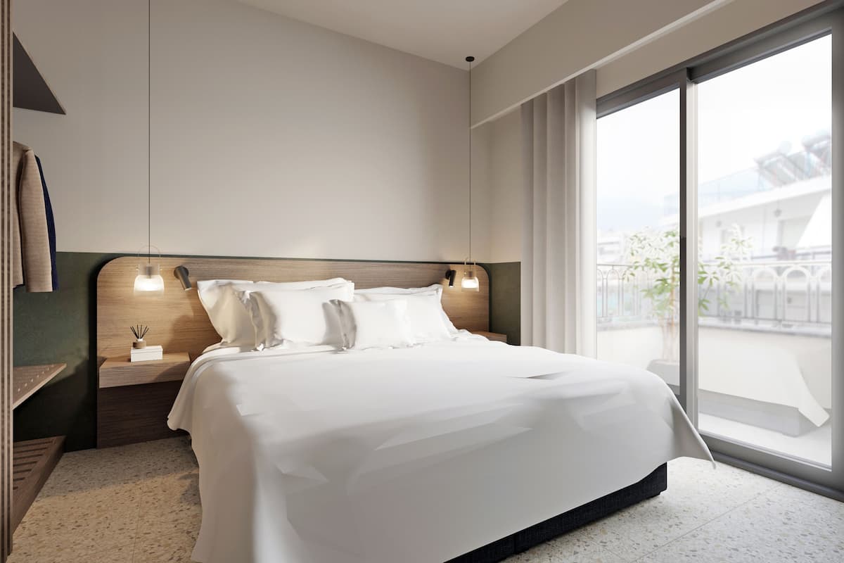 Ein modernes Hotelzimmer mit einem großen Bett, einem Nachttisch mit Lampe und Blick auf die Stadt durch große Fenster.