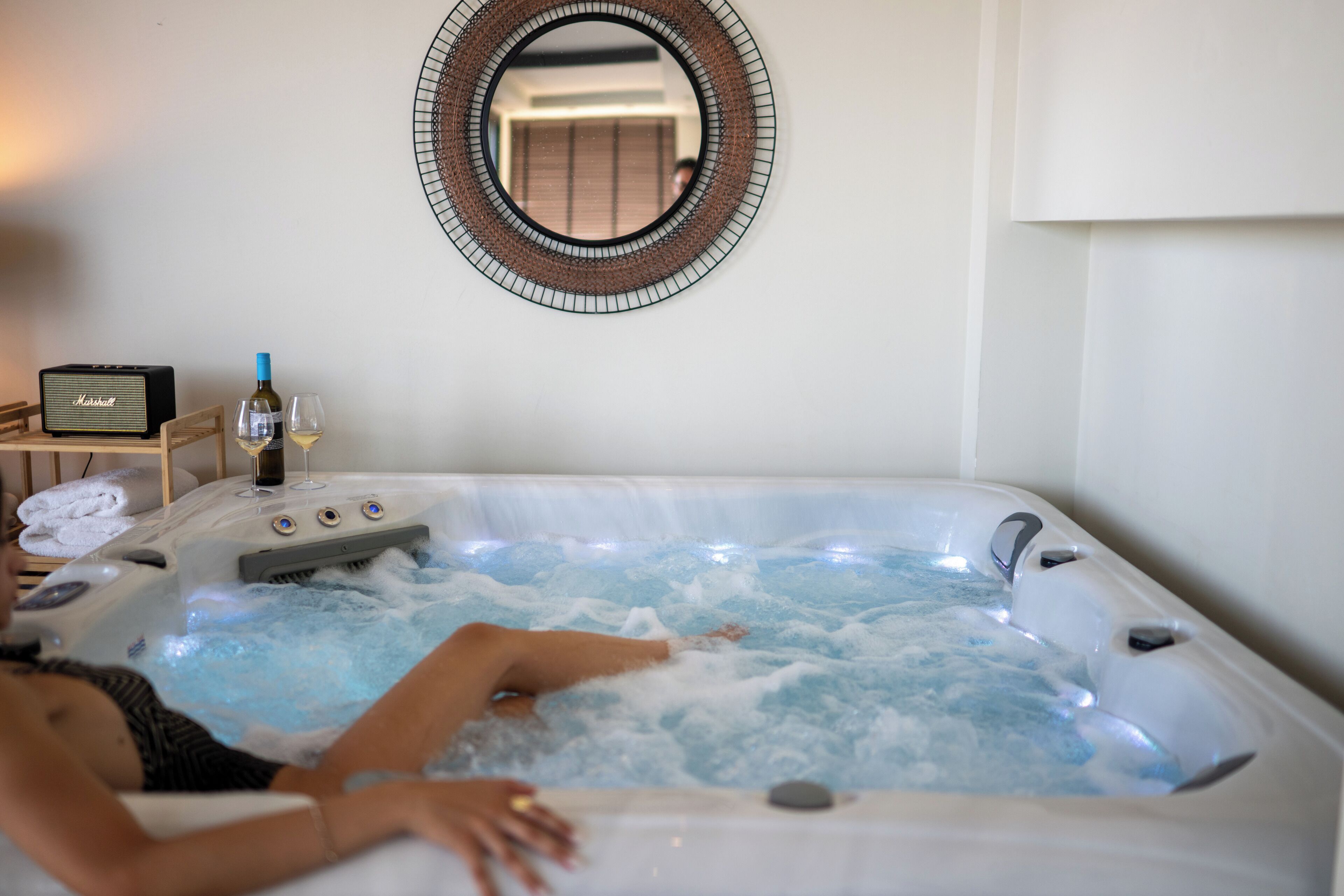 A person relaxing in a hot tub with a radio and a bottle of wine nearby.