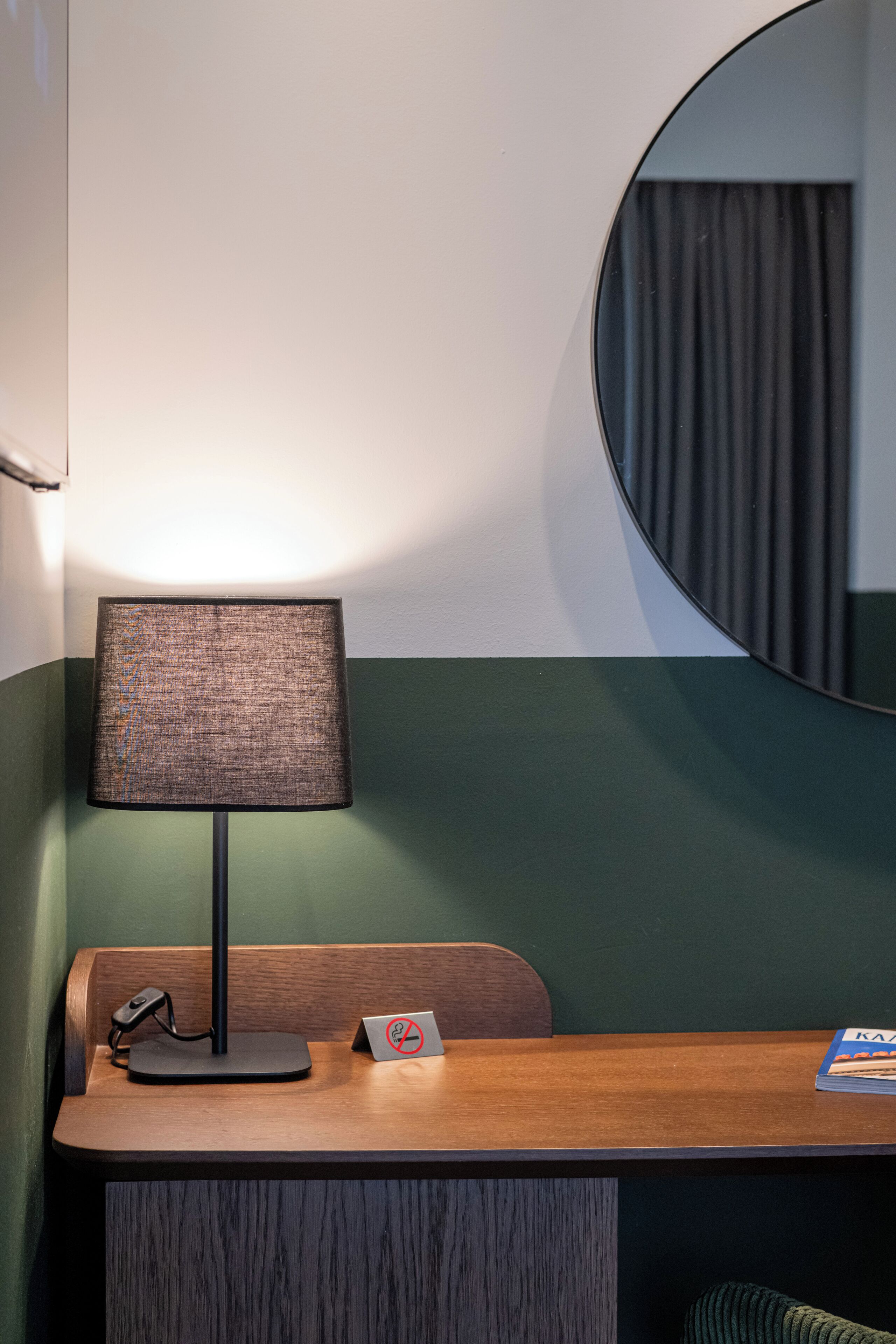 Een hotelkamer met een houten bureau, een lamp, een spiegel en een bordje met een rookverbodssymbool.