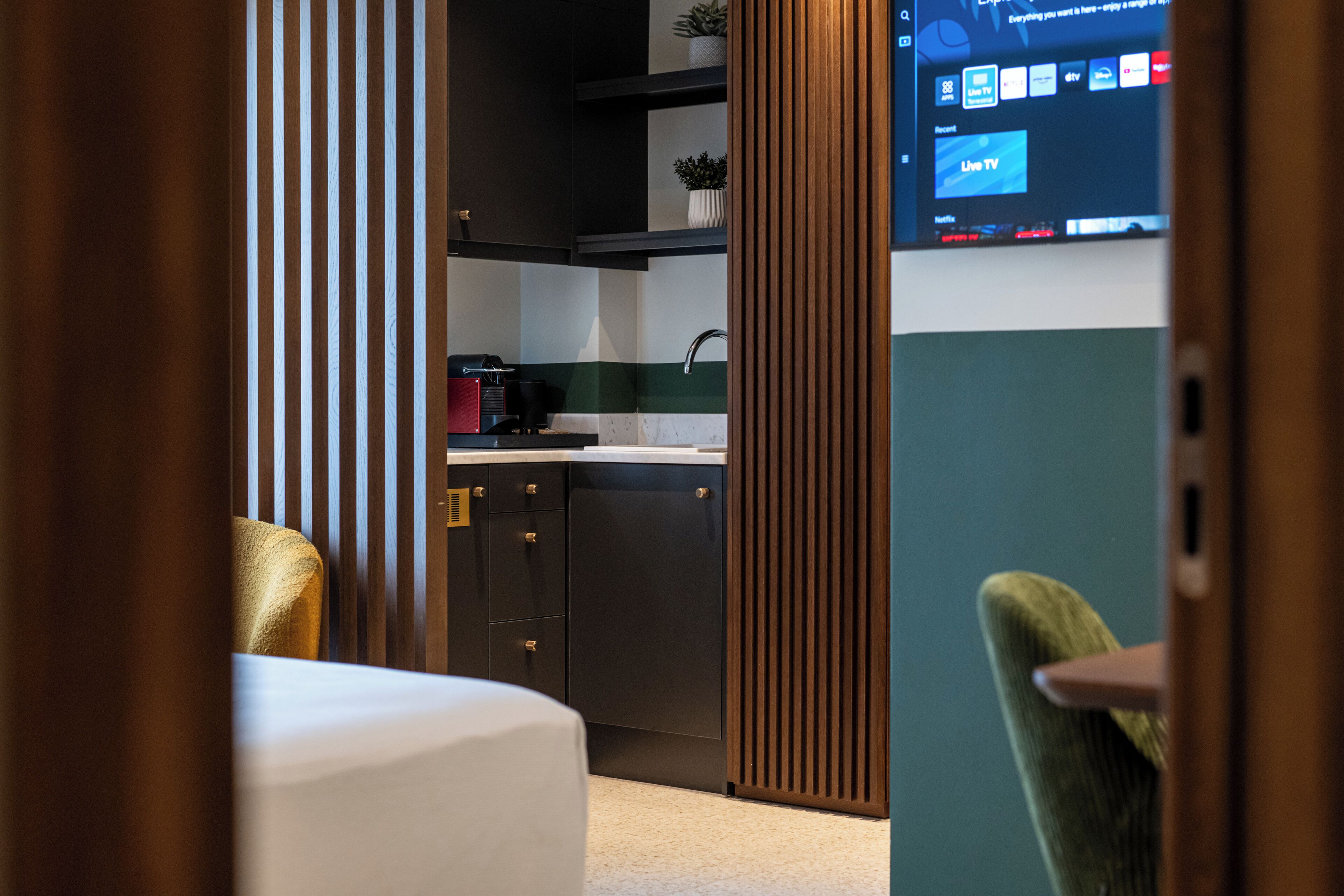 A modern hotel room with a bed, a desk, and a view of the kitchen area.