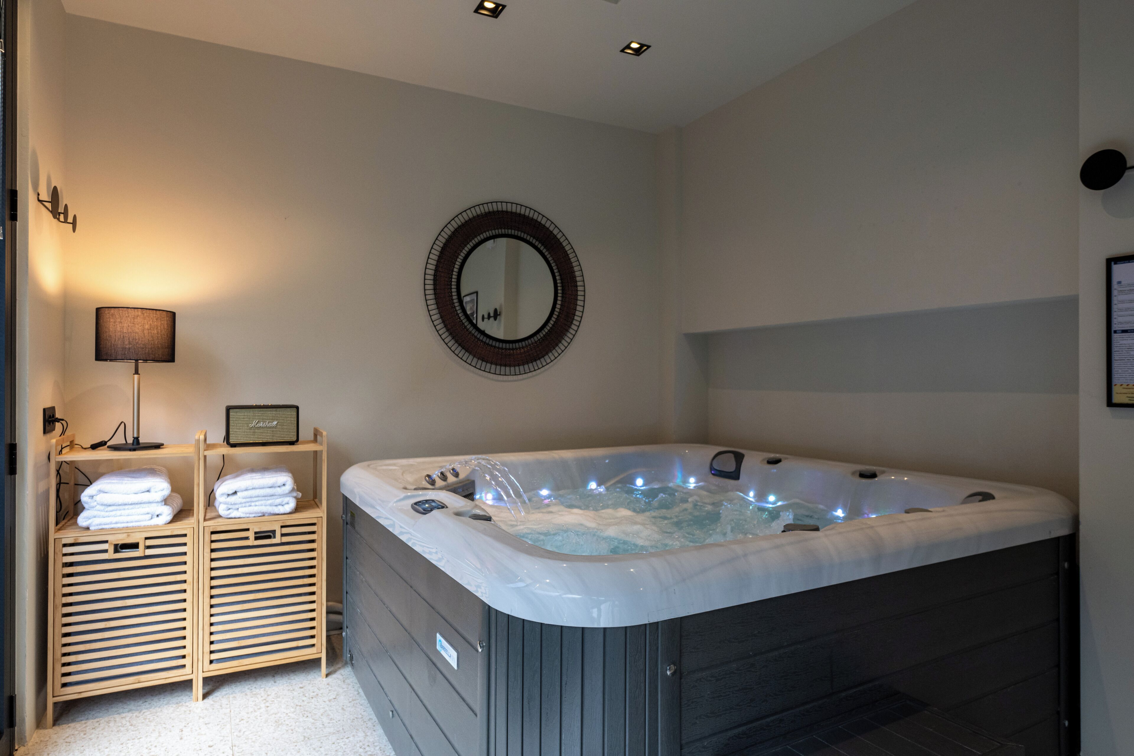 Ein Badezimmer mit Whirlpool, Holzregalen mit Handtüchern, einem Spiegel und einer Wandleuchte.