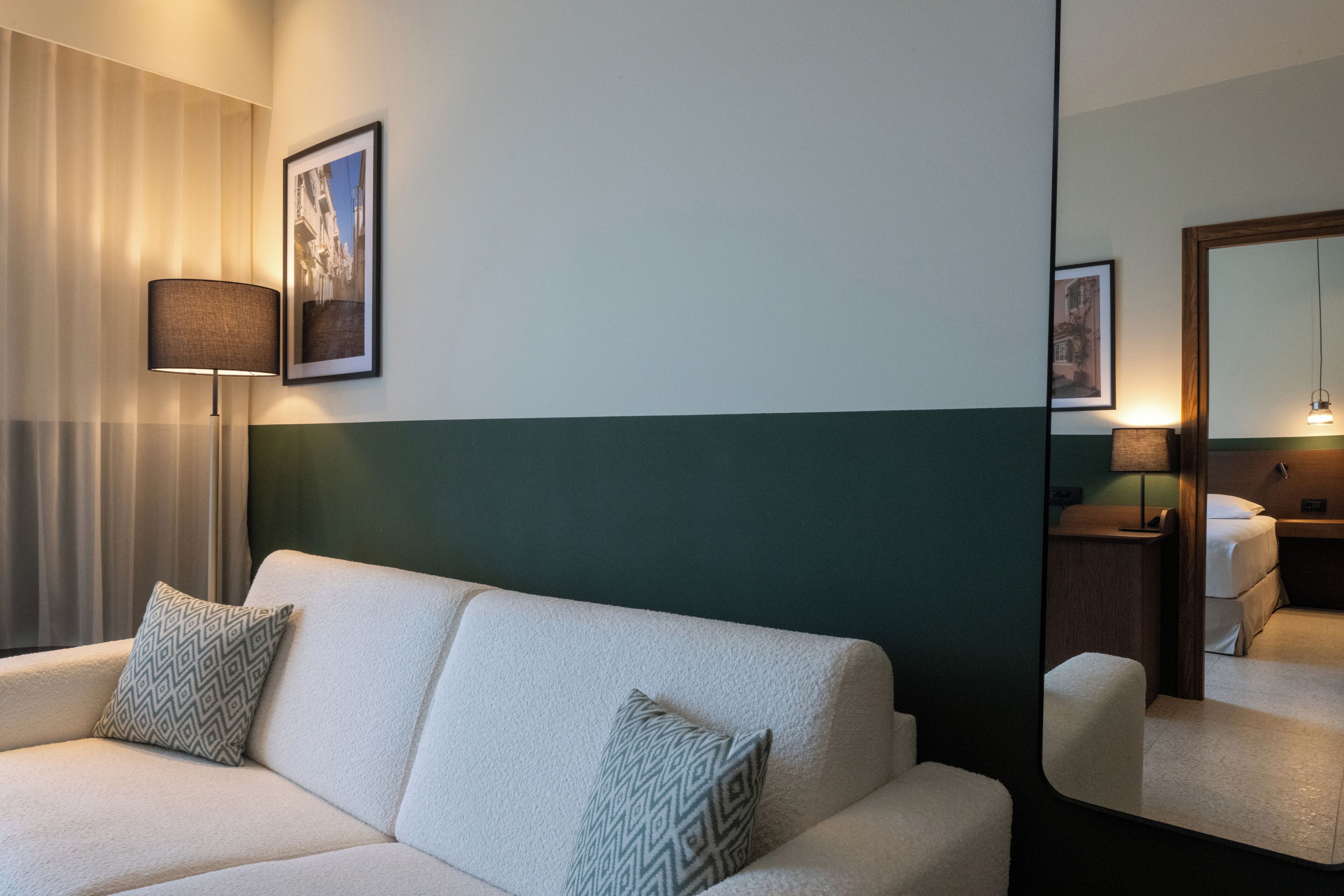 Habitación de hotel con sofá, almohadas estampadas, lámpara y espejo que refleja la habitación.