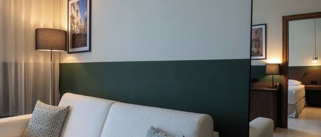 Habitación de hotel con sofá, almohadas estampadas, lámpara y espejo que refleja la habitación.