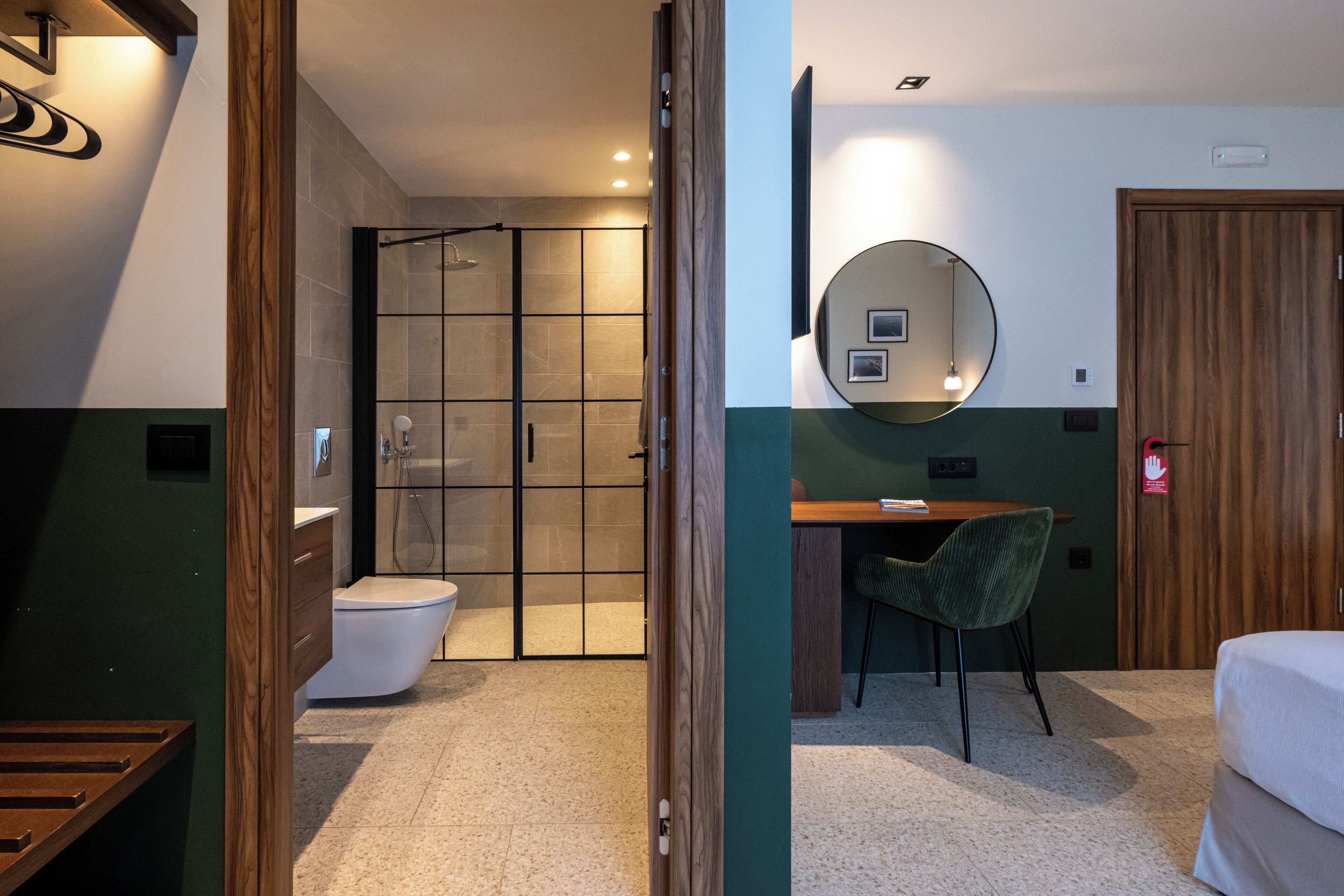 Moderni hotellihuone, jossa on suihku, wc ja työpöytä tuolilla.