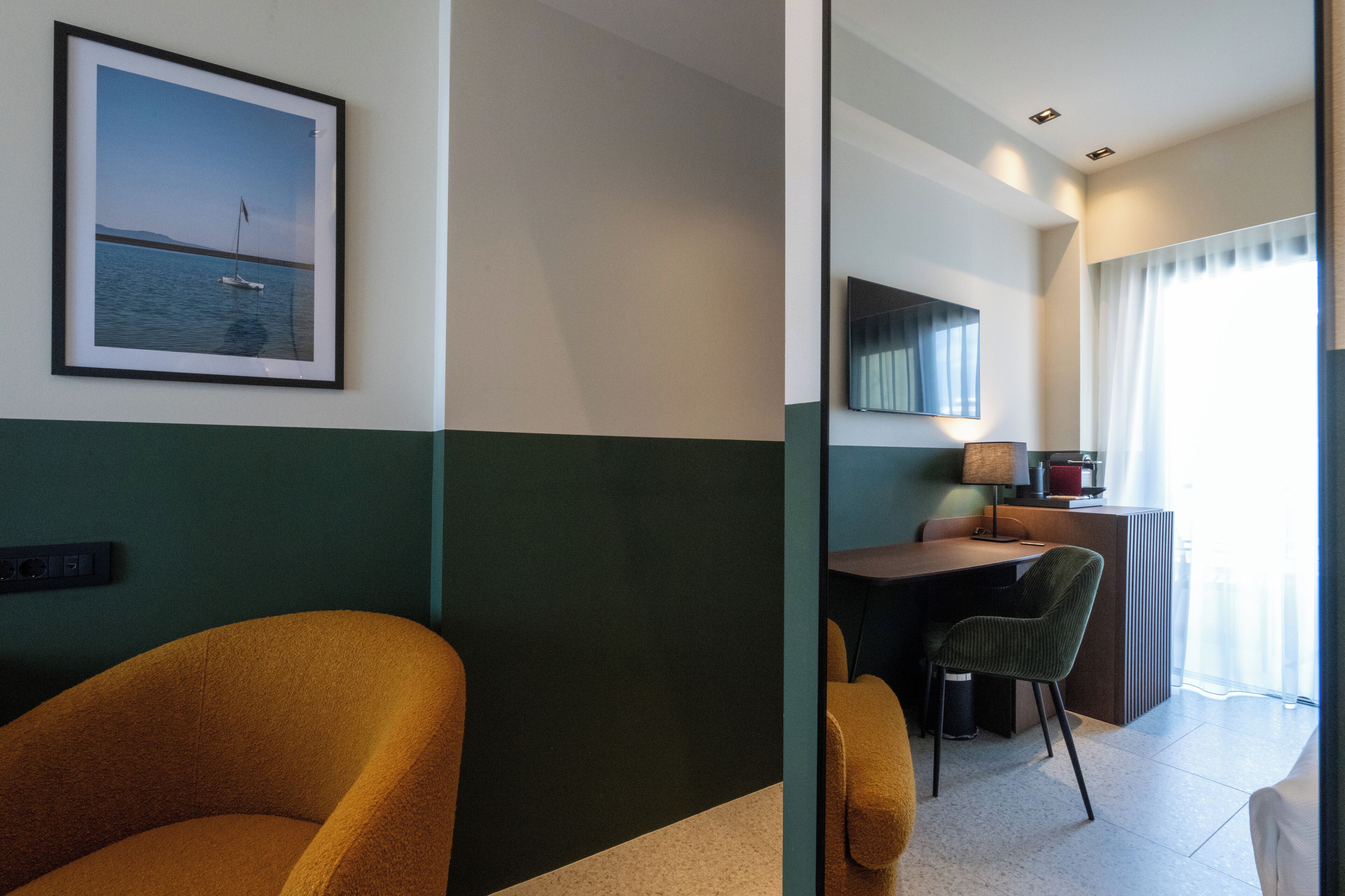 Habitación de hotel con cama, escritorio, silla, un cuadro en la pared y ventana con cortinas.