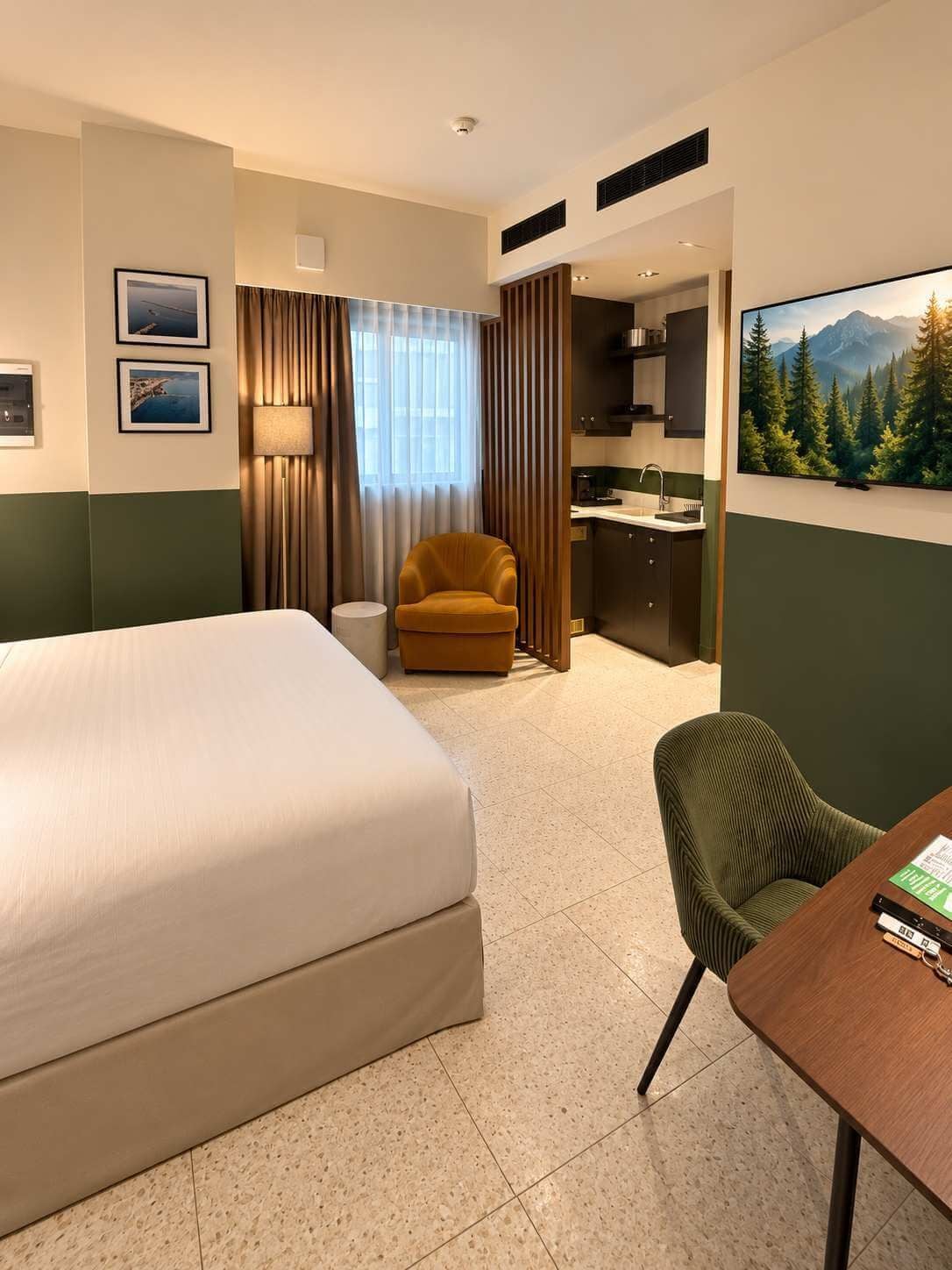 A hotel room with a bed, a desk, a chair, a lamp, a painting, and a view of a forest.