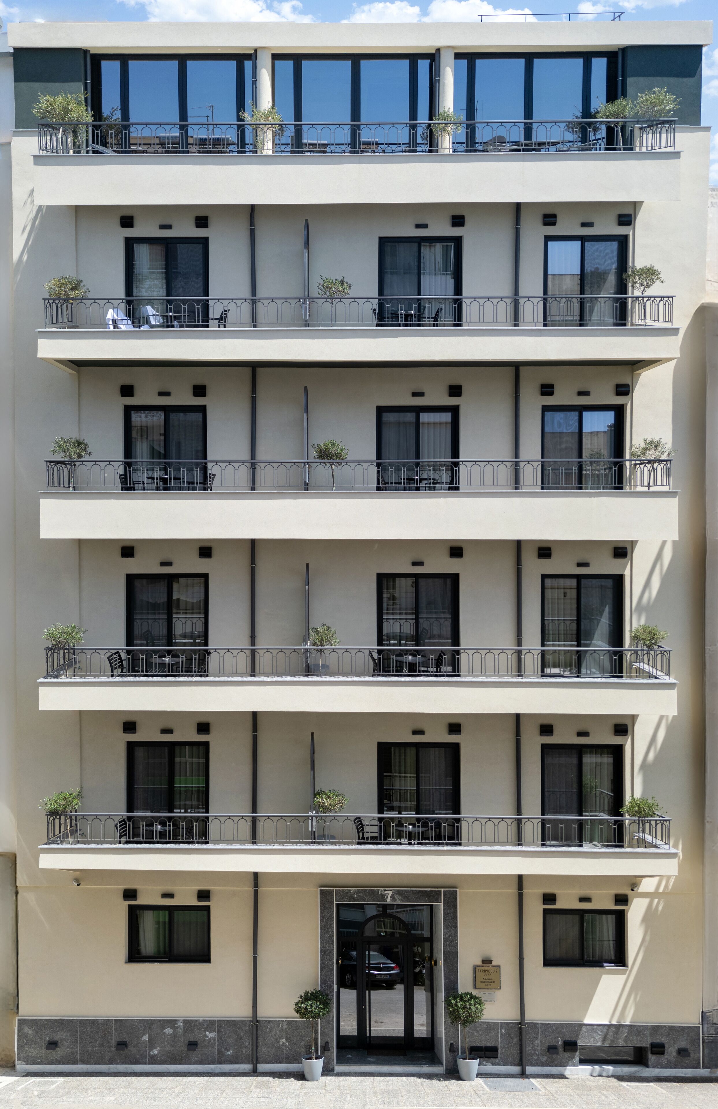 Et hotel med flere etager, altaner, krukker med planter og en klar himmel.