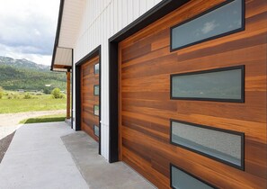 Un bâtiment moderne doté de grandes portes de garage en bois et d’un chemin en béton menant à l’entrée.