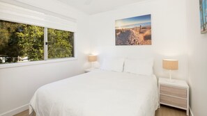 A bedroom with a large bed, two bedside tables with lamps, a window with blinds, and a wall-mounted picture. - Beachway - Pet Friendly - 2 Mins Walk to Beach (Berrara)