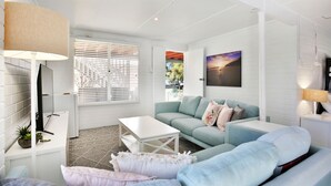 A modern living room with a light blue sofa, a white coffee table, and a TV on a white brick wall.