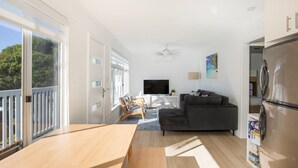 A modern living room with a large TV, a grey sofa, and a wooden dining table.