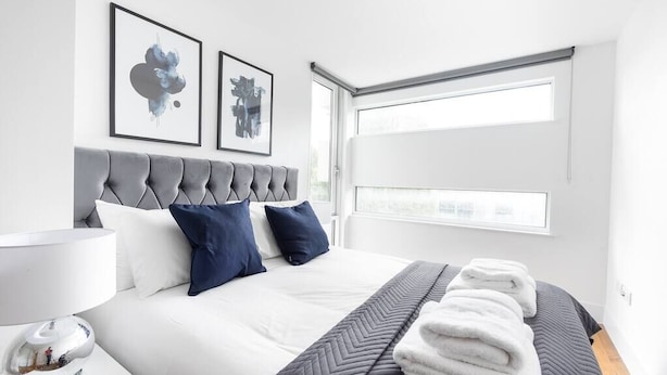 A modern hotel room with a large bed, grey and white bedding, a grey headboard, and two framed artworks on the wall. - PBC | One Bedroom Apartment with Balcony JT4 (London)