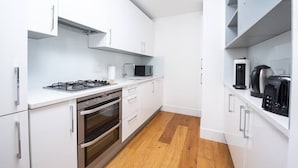 A modern kitchen with white cabinets, a gas stove, an oven, a microwave, and a coffee machine. - PBC | One Bedroom Apartment with Balcony JT4 (London)