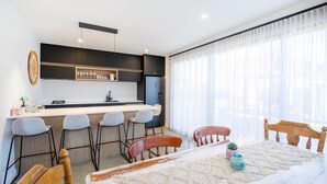 A modern kitchen with a bar area, bar stools, and a dining table with chairs. - Sandy Rays - 5 Mins Walk to Beach (Culburra Beach)