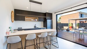 A modern kitchen with a bar area, a dining area with outdoor seating, and a view of the backyard. - Sandy Rays - 5 Mins Walk to Beach (Culburra Beach)