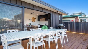 An outdoor dining area with a white table and chairs, a small potted plant, and a grill. - Sandy Rays - 5 Mins Walk to Beach (Culburra Beach)