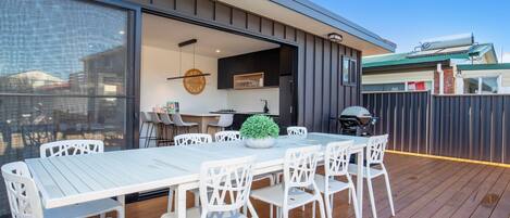 An outdoor dining area with a white table and chairs, a small potted plant, and a grill.