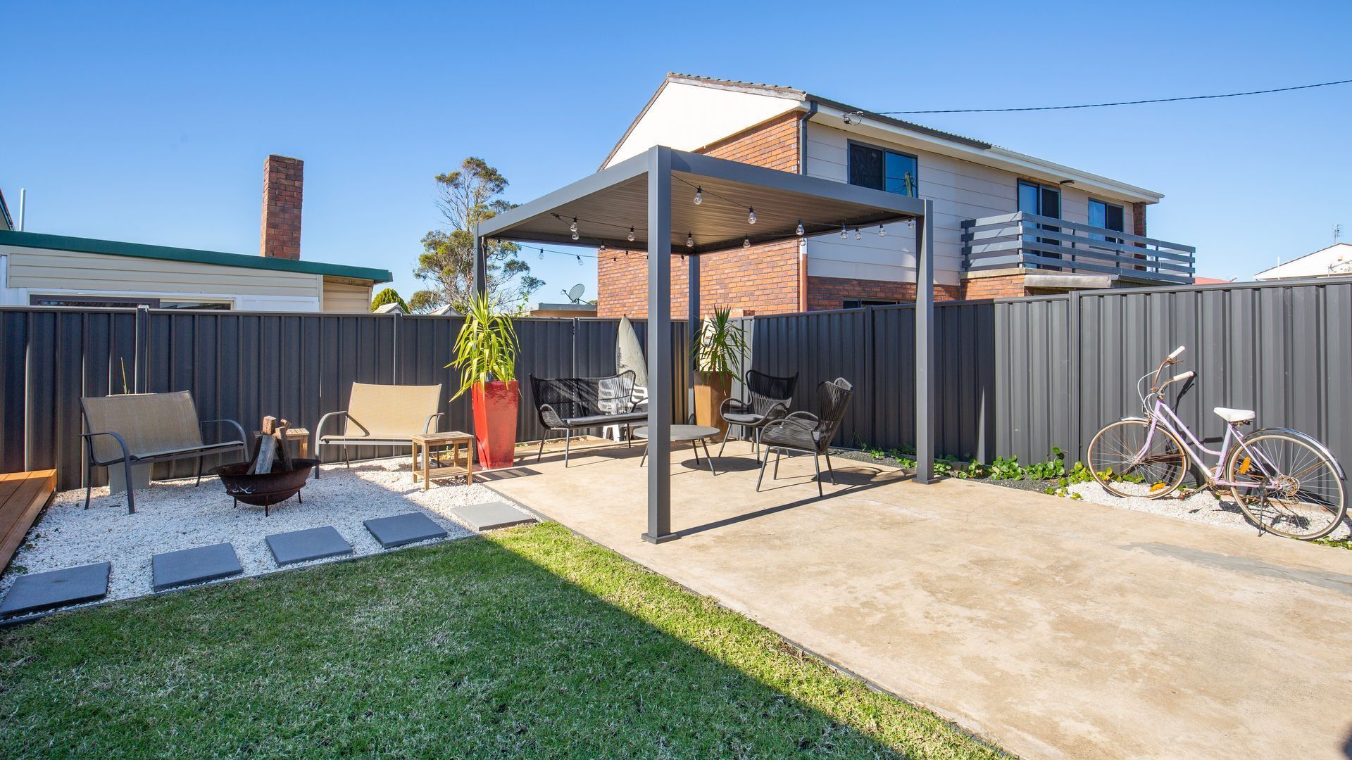 A backyard with a covered patio, outdoor furniture, a bicycle, and a well-maintained lawn.