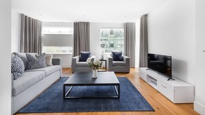 A modern living room with a sofa, two armchairs, a coffee table, a TV, and large windows. - PBC | One Bedroom Apartment with Balcony JT2 (London)