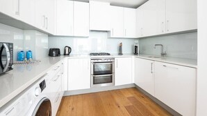 A modern kitchen with white cabinets, stainless steel appliances, and a built-in washing machine. - PBC | One Bedroom Apartment with Balcony JT2 (London)