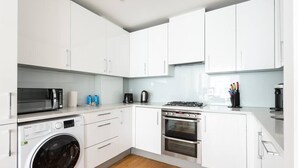 A modern kitchen with white cabinets, a washing machine, a stove, and a microwave. - PBC | One Bedroom Apartment with Balcony JT2 (London)