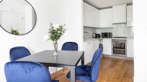 Une cuisine moderne avec des meubles blancs, une cuisinière et un four. On y trouve une table à manger avec des chaises bleues et un vase rempli de fleurs.