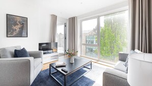 Un salon moderne avec un canapé, une table basse, un téléviseur et une grande fenêtre agrémentée de rideaux.